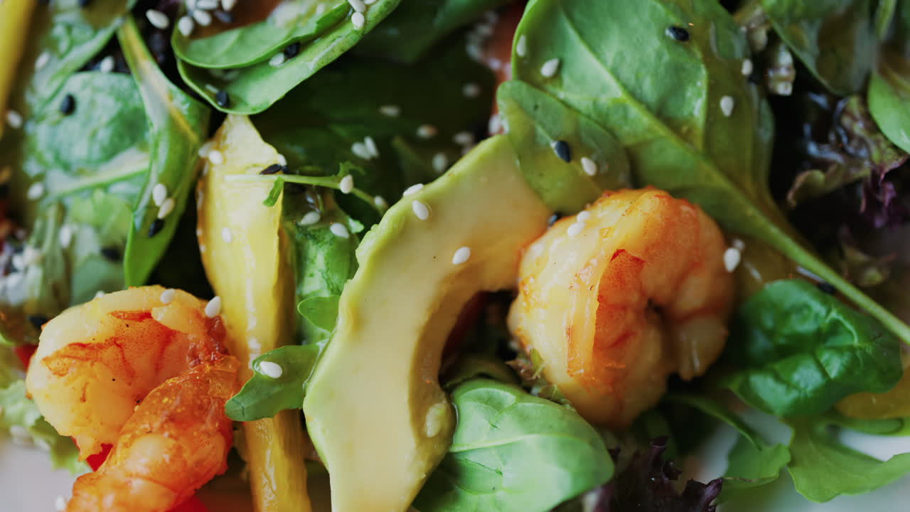 Close up of a salad with spinach, avocado, shrimp, and peppers on a white plate