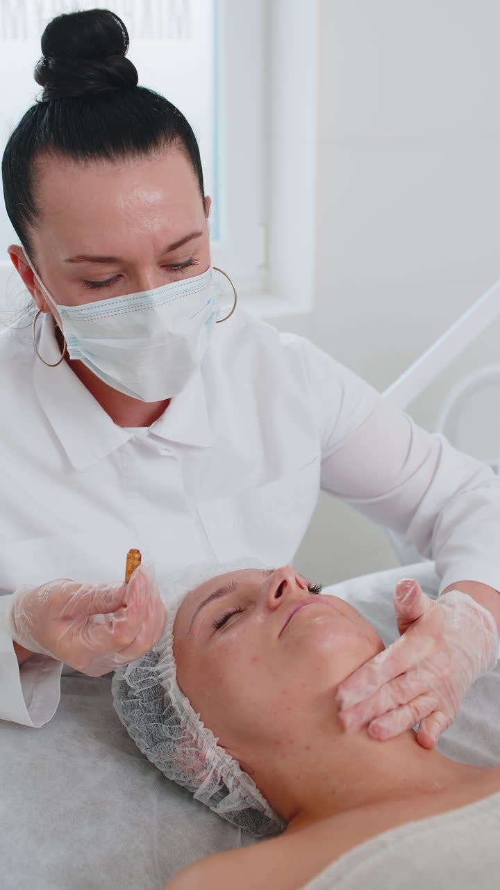 Cosmetologist applying moisturizing medical chemical peeling cream mask on young adult woman face