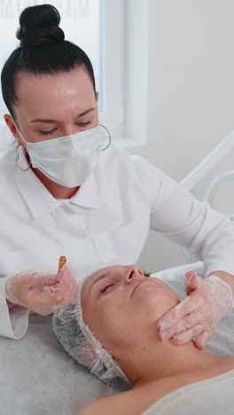 Cosmetologist applying moisturizing medical chemical peeling cream mask on young adult woman face