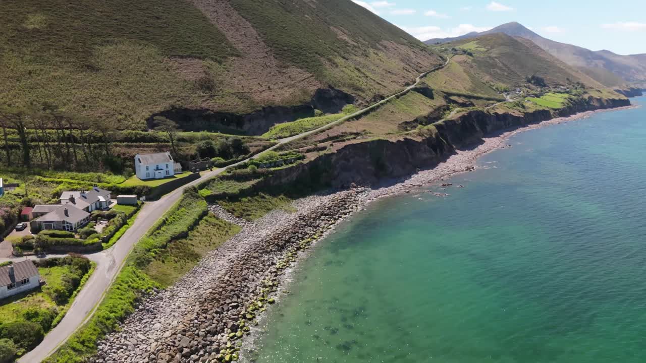 Aerial view of Rosbeigh, Ireland. Flying above beach and calm ocean along dramatic coastline, with rolling hills under clear summer skies. Peaceful coastal landscape.