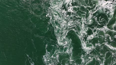 aerial overhead shot of ocean waves splashing and crashing during sunny day