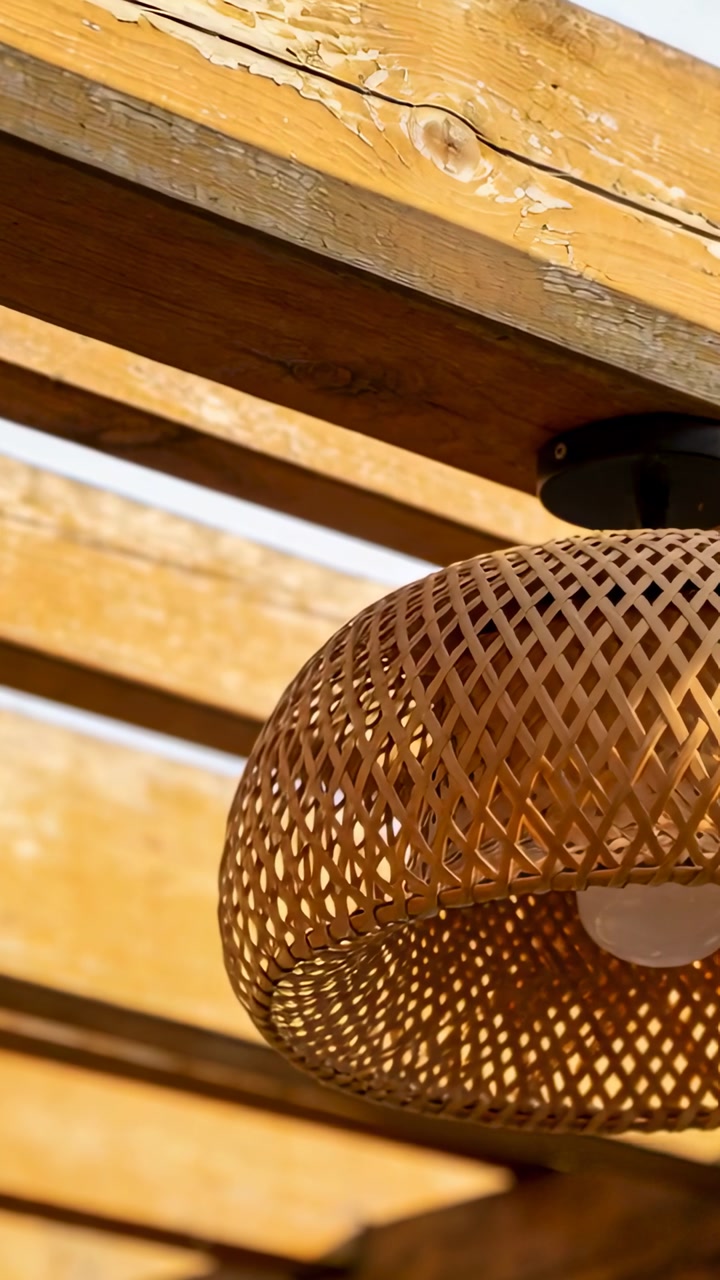 Vertical video: Tilting cam showing rattan lamp bare bulb and black mount under pergola, copy space