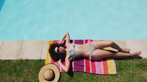 mixed race woman lying on blanket sunbathing by the pool