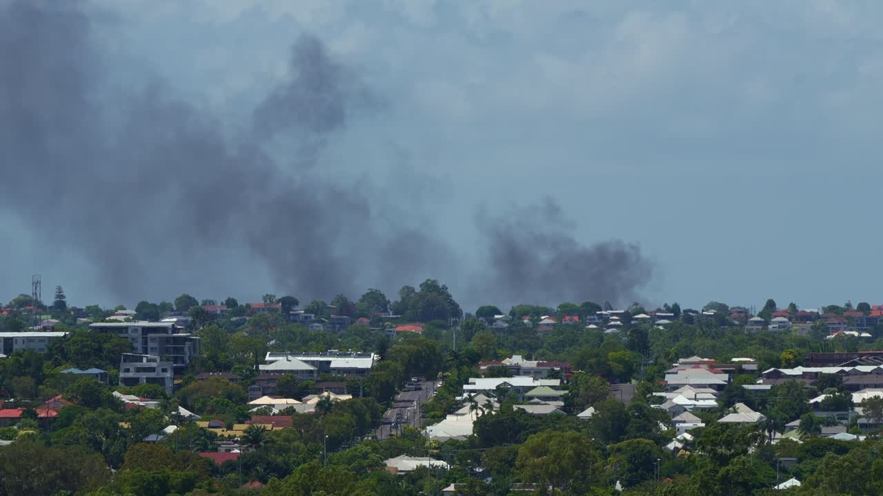 A commercial building in Kedron is engulfed by a structure fire, sending a thick column of smoke into the air, visible from Bowen Hills.