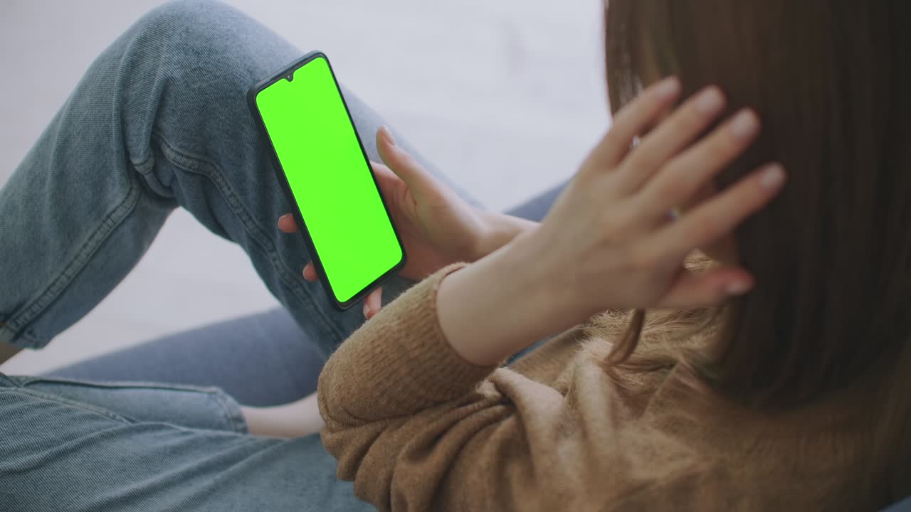집에서 소파에 누워있는 여성은 초록색 모형 화면의 스마트폰을 사용하여 스와이프, 스크롤 제스처를 수행합니다. 휴대 전화, 인터넷, 소셜 네트워크 브라우징을 사용하는 남자. 시점 카메라
