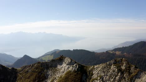 short aerial orbit with hikers standing out as shadow on summit "la cape au moine" with lake léman in the background, vaud - switzerland