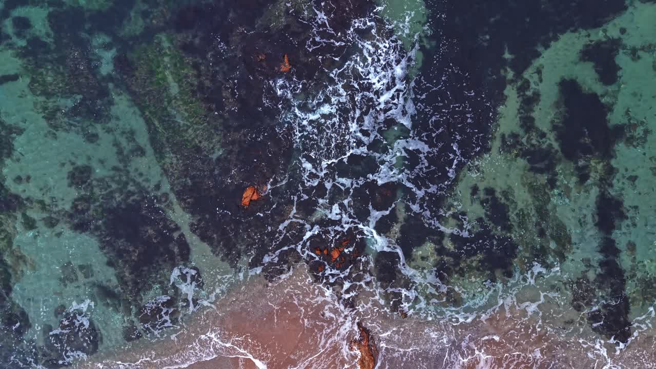 Aerial view of waves crashing on the shore with rocky formations