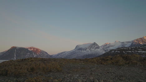 Aerial-drone-push-in-over-hill,-revealing-bay,-mountains-in-Tromvik,-Kvaloya,-Northern-Norway