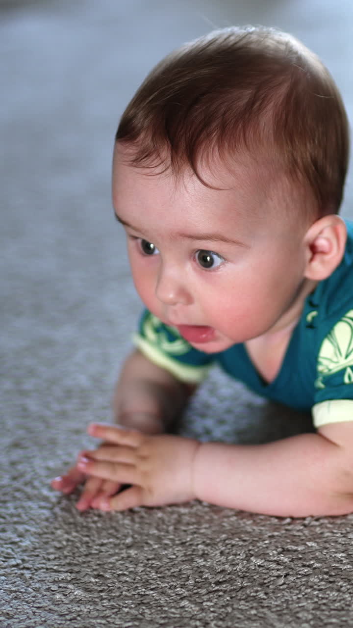 Little child banging his hands over the floor happily. Beautiful kid lies on a carpet looking up with interest. Vertical video