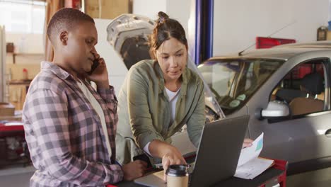 Video-of-two-diverse-female-car-mechanics-using-laptop-and-smartphone,-searching-for-car-parts