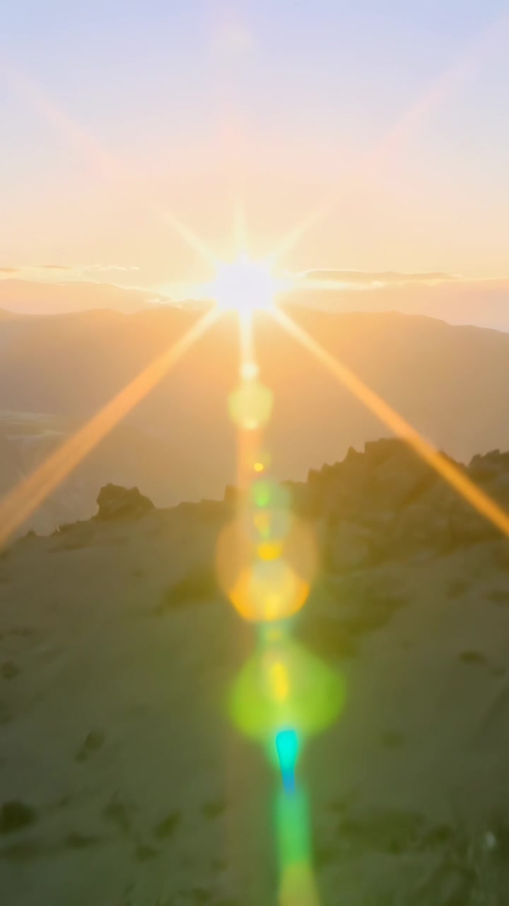 Vertical video: Emerging sun causing starburst rays across rocky slope above ridge with lens flare