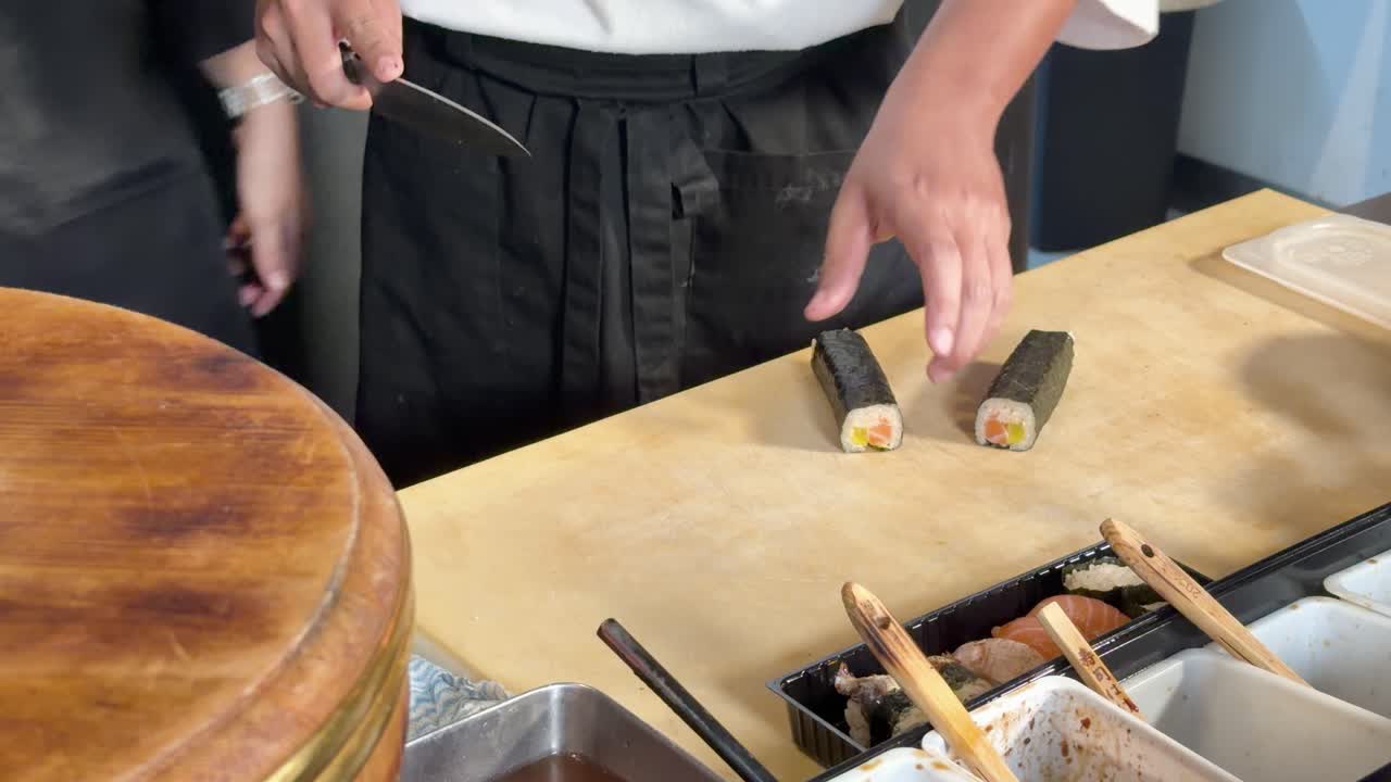 Detailní záběr profesionálního sushi šéfkuchaře krájejícího maki rolku na dřevěném pultu se stabilní kamerou