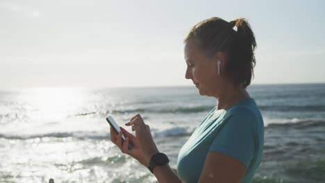 mujer mayor usando un teléfono inteligente mientras corre en un paseo marítimo