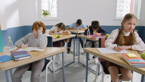 grupo multiétnico de estudiantes sentados en pupitres en clase de inglés levantando los brazos para responder a la pregunta 1 del profesor