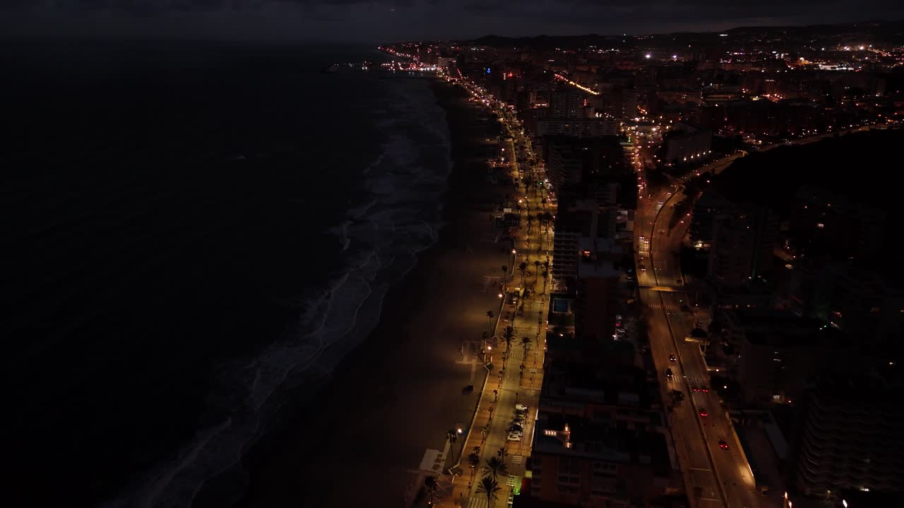 Drone capturing the illuminated coastline of Torreblanca, Spain, at night, showcasing the lights of the city and the dark sea waves of the Mediterranean sea crashing on the beach
