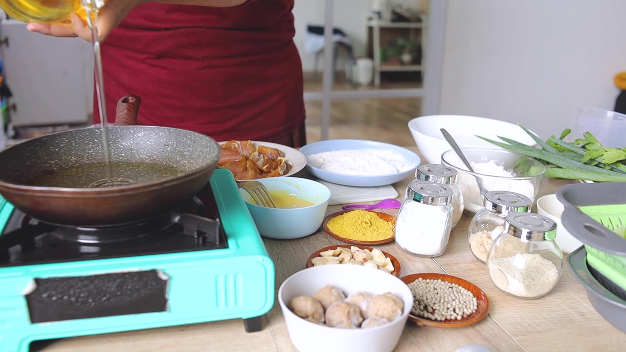 Koki menuangkan minyak goreng dari botol ke wajan panas di atas kompor gas portabel di dapur