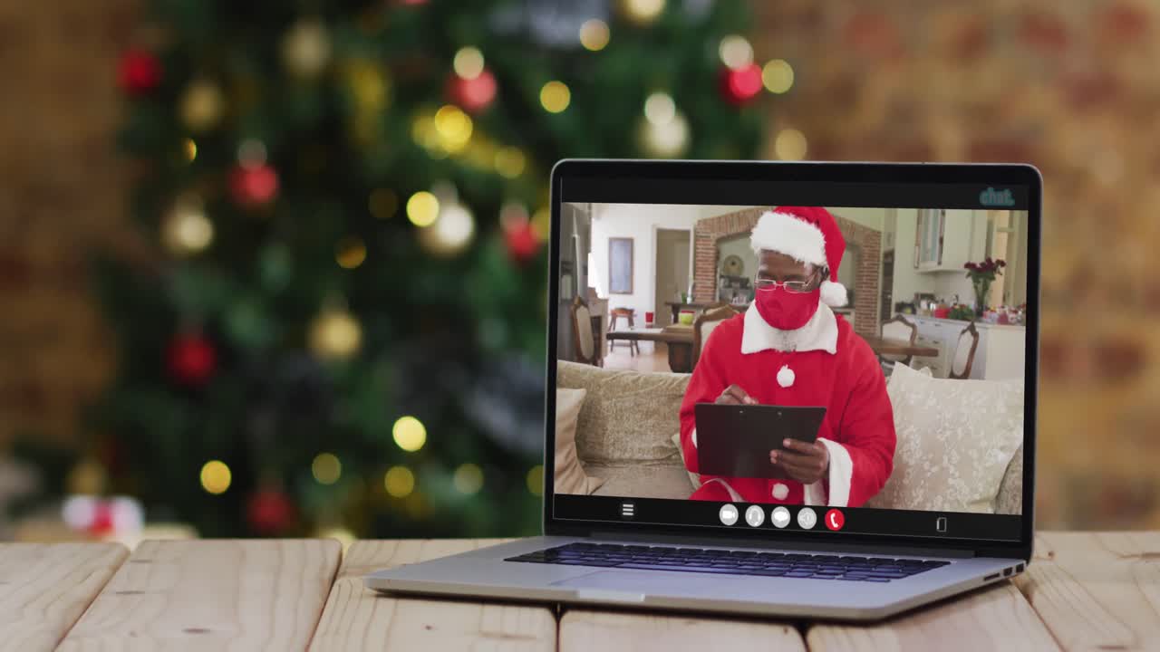 santa afroamericano con máscara de cara en una videollamada , con árbol de navidad
