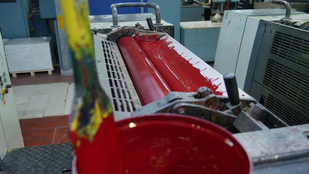 Pot of red paint with a roll behind preparing to print some templates for the labels, mass production machine