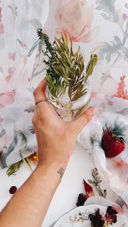 hand holding a glass with dried flowers and still life arrangement