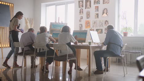 un grupo feliz de personas mayores pintan cuadros juntos en clase.