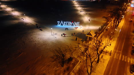 sign letters zakopane with a decoration of red santa cap. people walk near the illuminated decor in the square. aerial view.