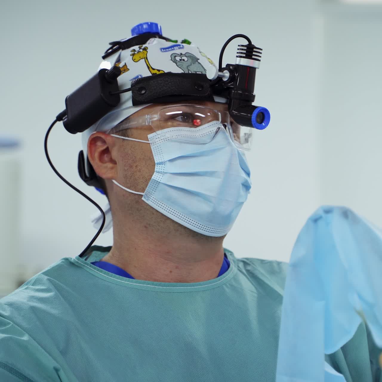 Experienced medic in device glasses, cap and mask moving the instruments looking ahead at the screen. Portrait of a focused doctor at procedure