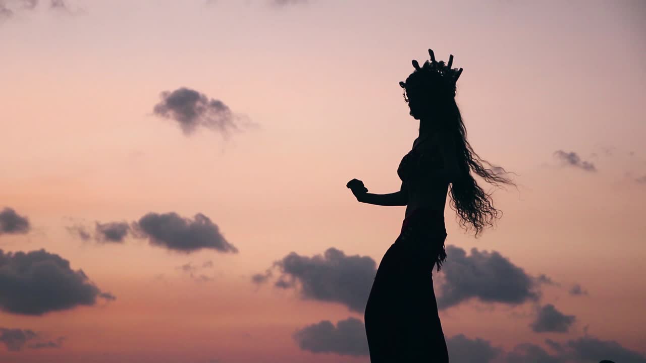 Close up of sexy, elegant and erotic arabian woman performing belly dance on the beach during golden hour. Silhouette. Side view