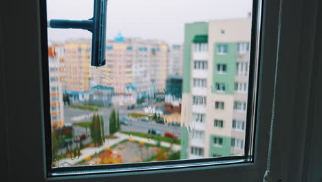 cleaning window in the city. man holding household brush and cleans window from outside. view from indoors. urban buildings background.
