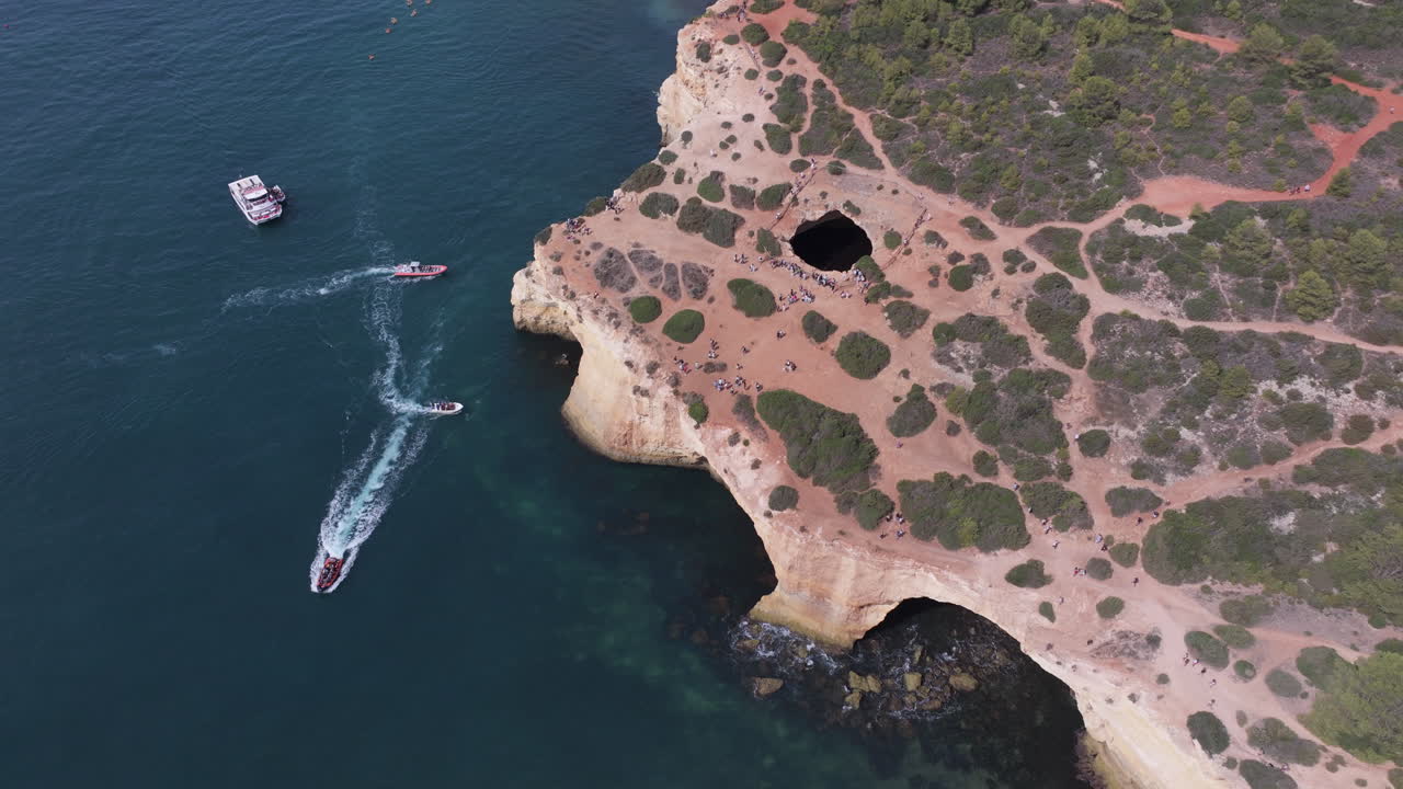 Aerial drone view of the Benagil Sea Cave and Atlantic Ocean coastline in Algarve, Portugal, Europe. Multiple tour boats crossing paths, concept shoot on mass tourism, preservation and overtourism