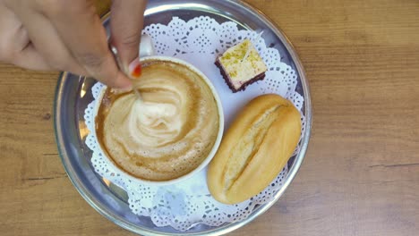 cerca de una taza de capuchino, una rebanada de pastel y un pan en una mesa de madera