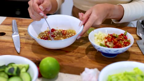 hands mix chili, garlic, and other ingredients in a bowl on a wooden countertop with fresh produce
