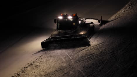 snow groomer pistenbully working at night in the dolomites, italy, lights on and grooming the slopes