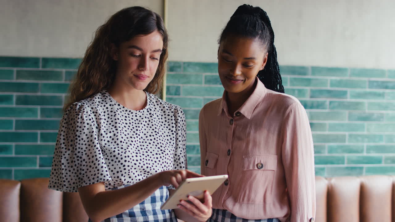 dos dueños o personal femenino sonrientes mirando una tableta digital en una cafetería o cafetería