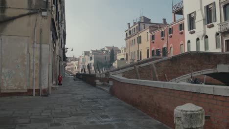 Canal-side-walkway-in-Venice-with-bridge,-Italy