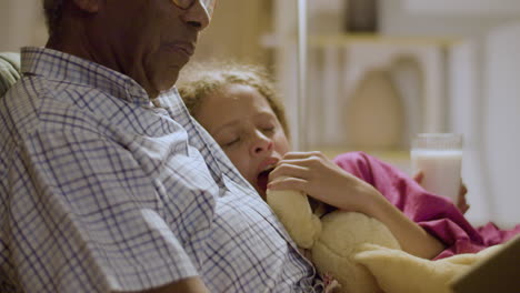 cute young girl listening to grandpa reading goodnight stories