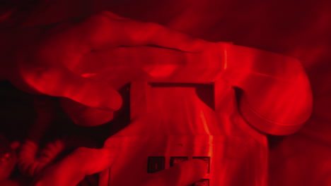 male hands holding tight a vintage white telephone handset in a hotel room with red light