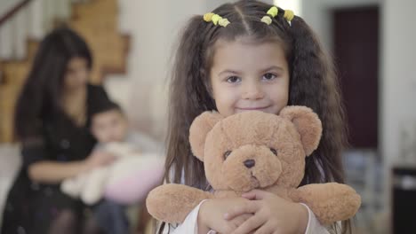 close-up of a smiling middle eastern girl with brown eyes and curly hair holding the teddy bear and looking at the camera