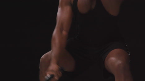 close up studio shot of male athlete training in fitness vest using battle ropes shot against black background 2