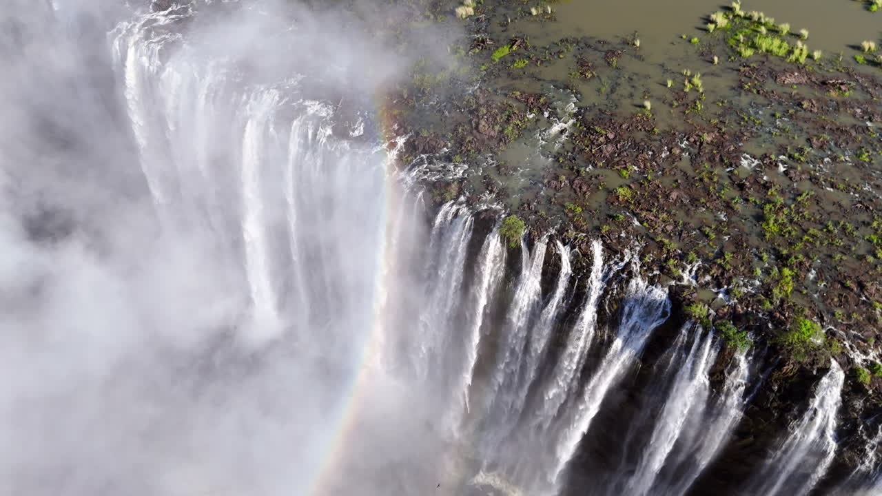 Aerial view of Victoria Falls with powerful waterfall plunging into gorge, mist rising above lush green forest, dramatic natural wonder and iconic travel destination in Africa