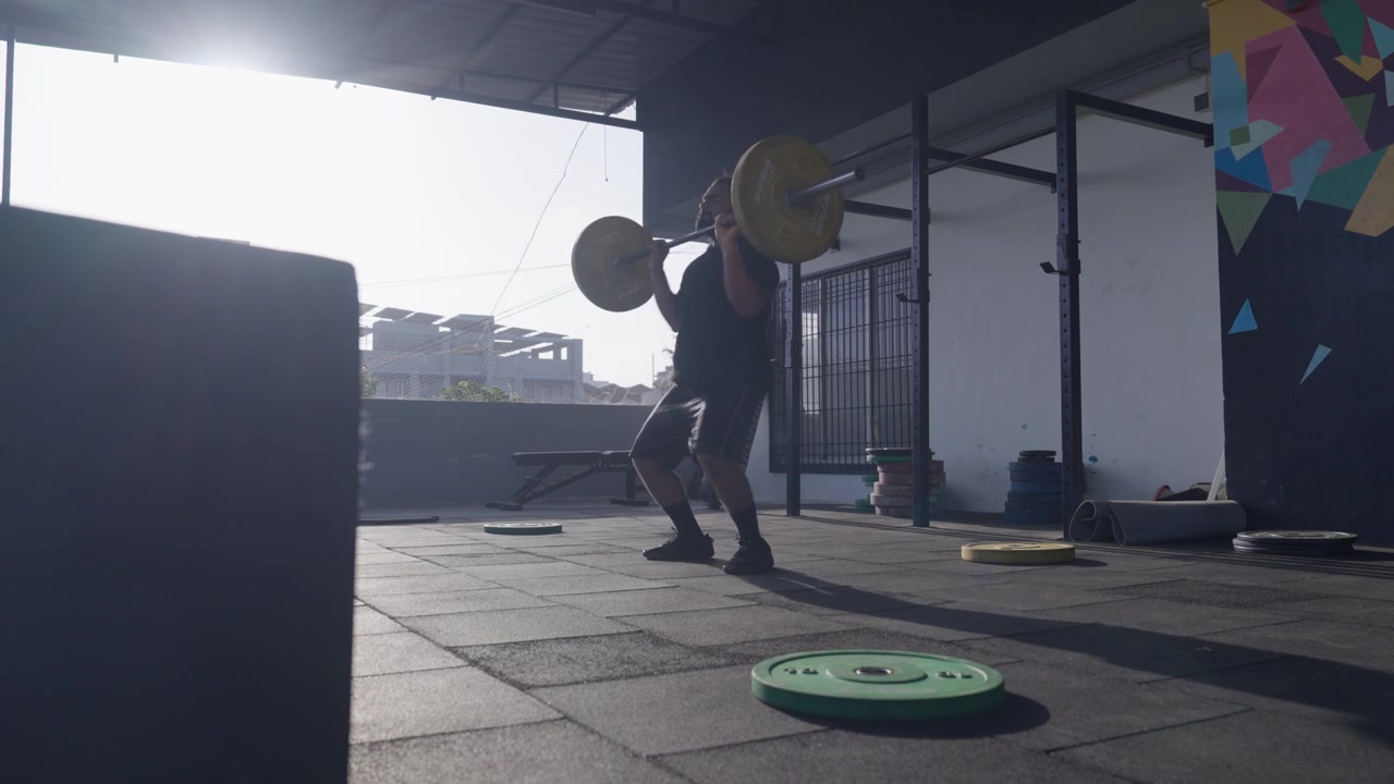 Brodaty sportowiec z Azji Południowej wykonuje zarzut siłowy przed upuszczeniem sztangi olimpijskiej na talerze bumperowe podczas treningu funkcjonalnego. Kolekcja: WORKOUTSERIES2026