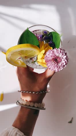 hand holding a glass of water with lemon and flowers