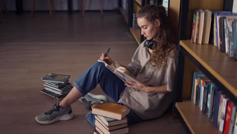 student in headphones sitting against bookshelf with a books on the floor