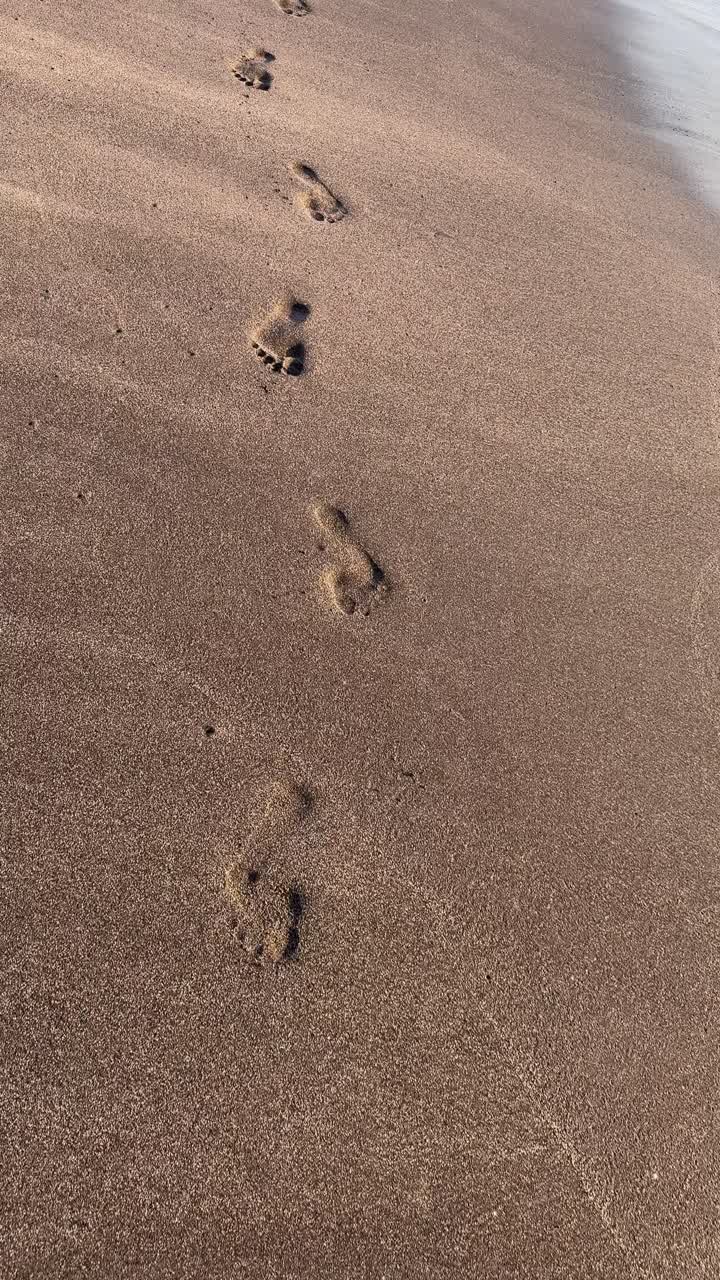 Pegadas na areia molhada levando em direção ao oceano