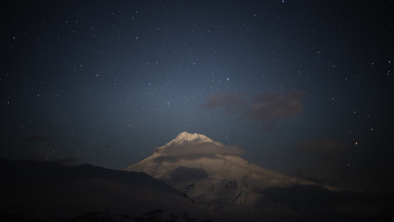 Montagnes enneigées sous un clair de lune éclatant avec des nuages traversant le ciel, la Voie lactée apparaît dans l'obscurité.