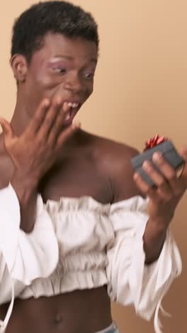 happy transgender african person receiving a gift on beige background