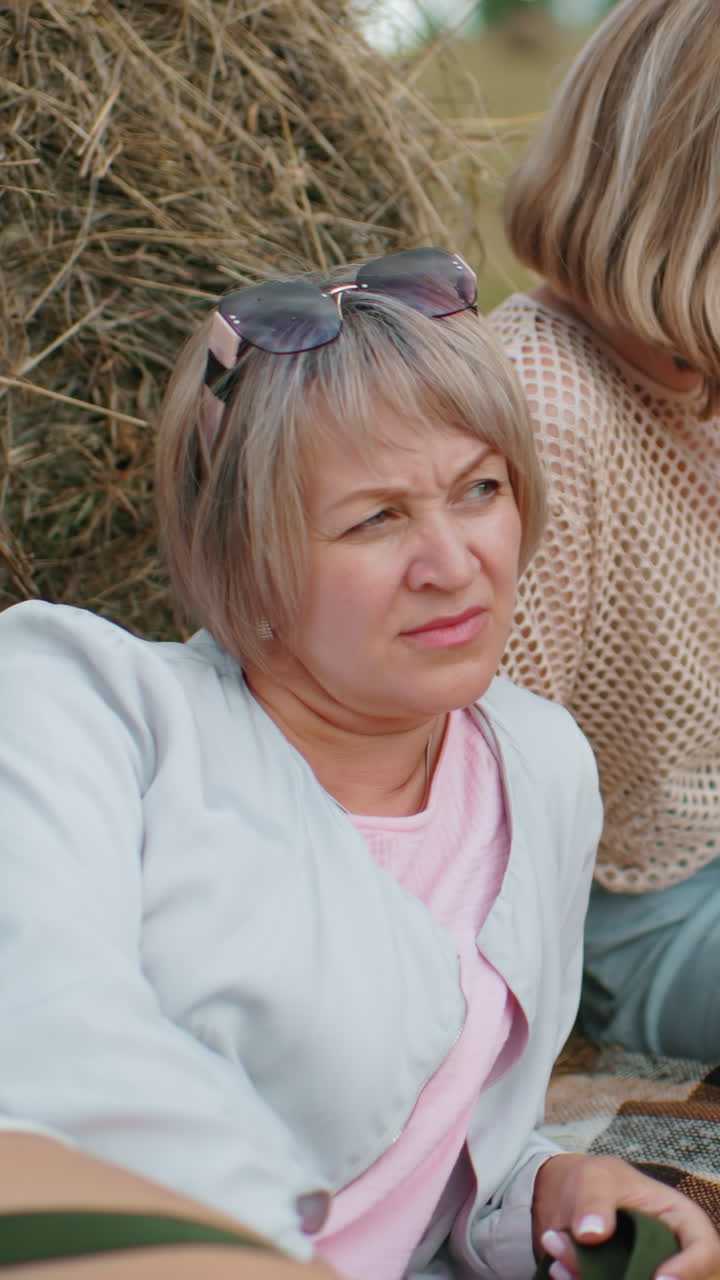 가족은 야외에서 조용한 순간을 즐기고, 야외에서 풀 근처에서 휴식을 취하고, 사려 깊은 여자가 멀리 쳐다보고, 다른 한 명은 뒤로 기대고, 아이는 읽기 위해 누워 있습니다.