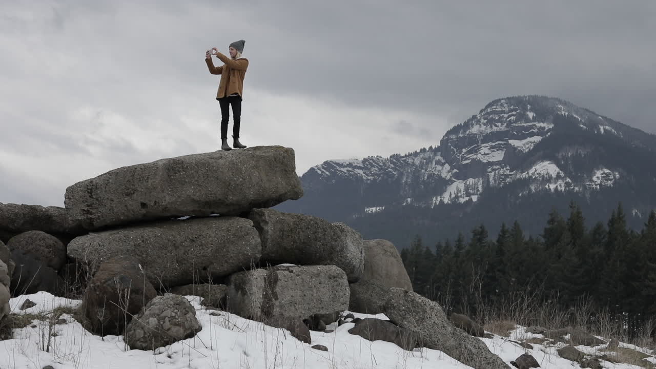 A girl takes pictures of the snowy mountains around her.