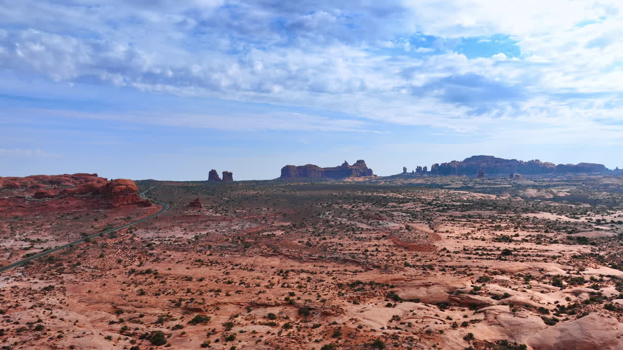 Rising above the dry deserted land with little bushes of lichens growing on. Majestic red canyons at backdrop. The Arches National Park, Utah, USA