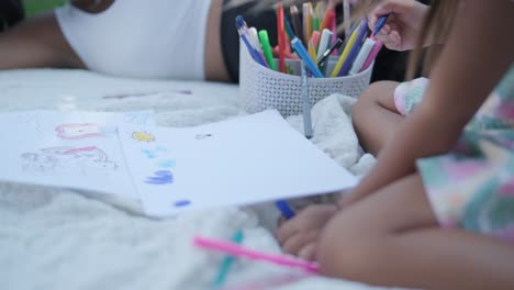 a mother and her young daughter sit on a blanket in the backyard, engaging in a drawing activity together. the outdoor scene captures a peaceful family moment, fostering creativity and bonding.