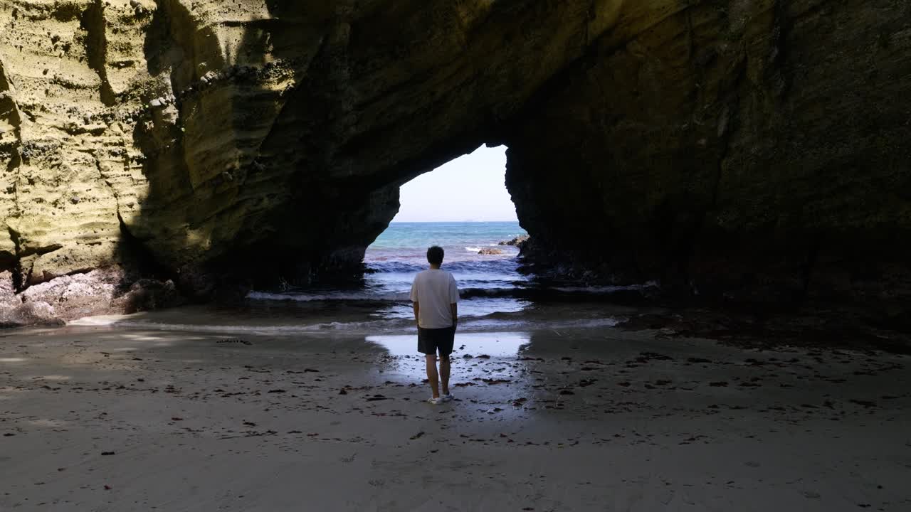 Male traveler walking towards ocean inside dark sea cave